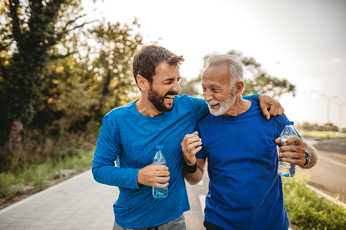 Senior man and younger man walking happily together outside holding water bottles