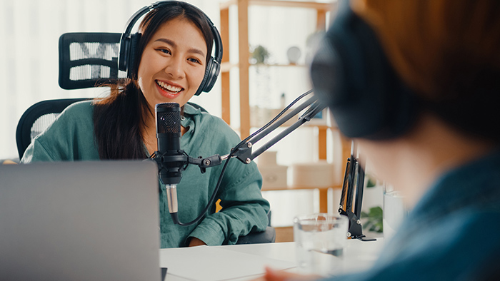 Two people sitting at table with headphones recording a podcast