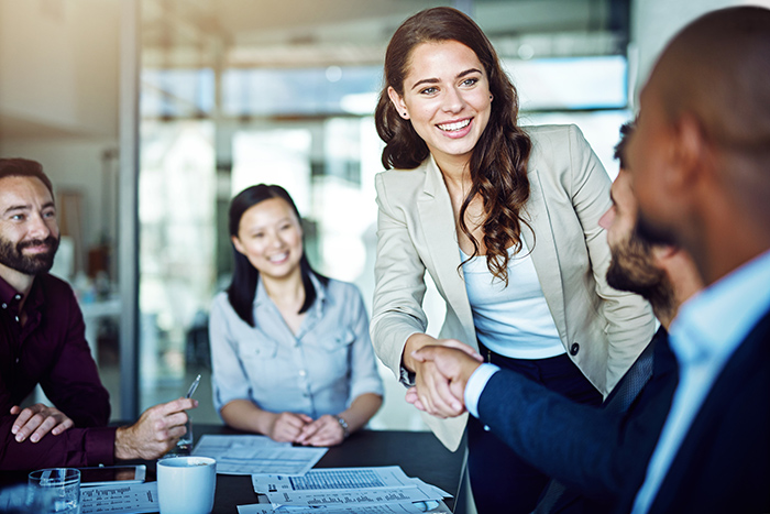 Woman and man shaking hands at conference table with people blurred in background
