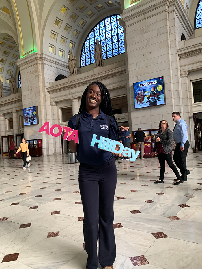 Woman smiling holding AOTA Hill Day signs inside building