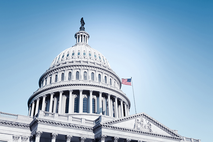 Outside view of US Capitol rotunda against blue sky with American flag waving on pole