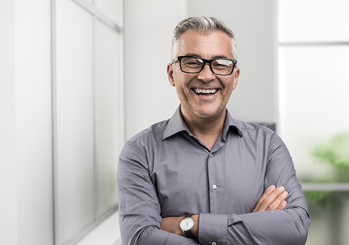 Smiling man wearing glasses with arms crossed looking into camera