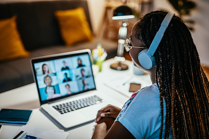 Young woman wearing headphones listening to virtual Zoom school lesson on laptop