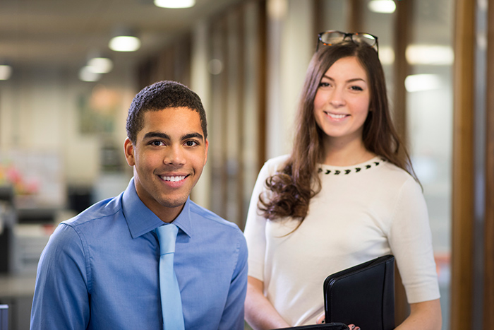 Male and female professionally dressed fieldwork students smiling at camera in office building