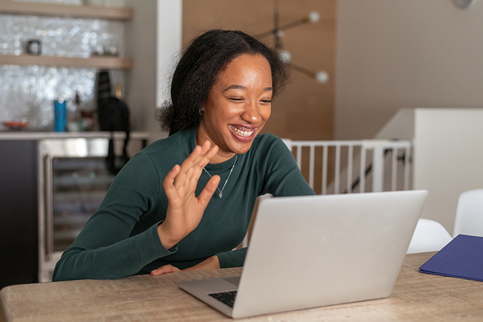 Young woman waving into laptop camera during virtual learning