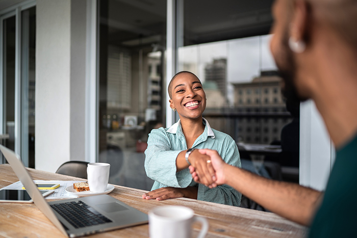 Woman sitting at table with coffee shaking hands with man using laptop