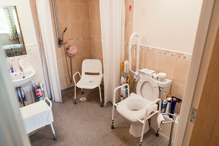 Adapted home bathroom with chair in the shower and toilet seat cover with grab bars
