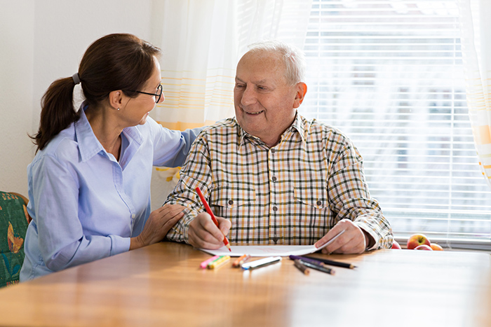 Senior man holding red pencil with female occupational therapist working on handwriting