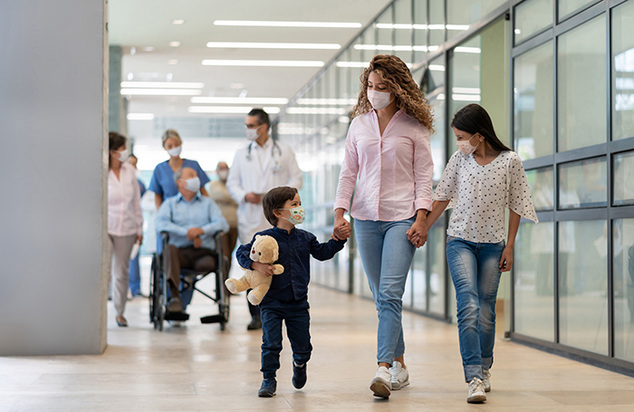 Woman with two small children wearing face masks walking through hospital
