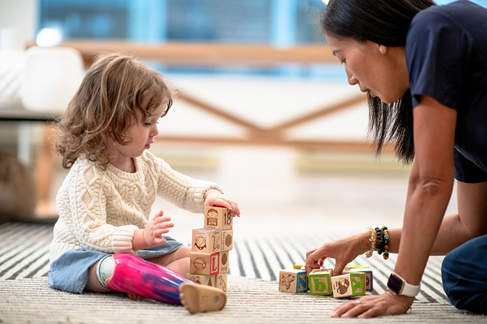 Female occupational therapist sitting on floor with toddler with prosthetic leg playing with building blocks