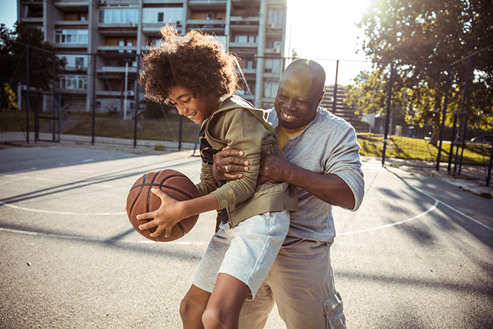 Man playing basketball outside with young kid