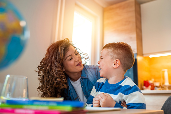 Woman sitting at table looking at laughing young boy sitting next to her