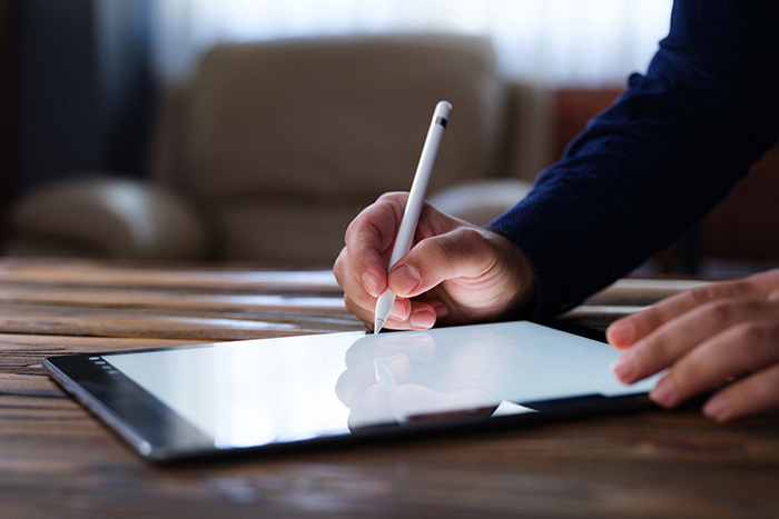 Male hands holding stylus pen writing on tablet on desk
