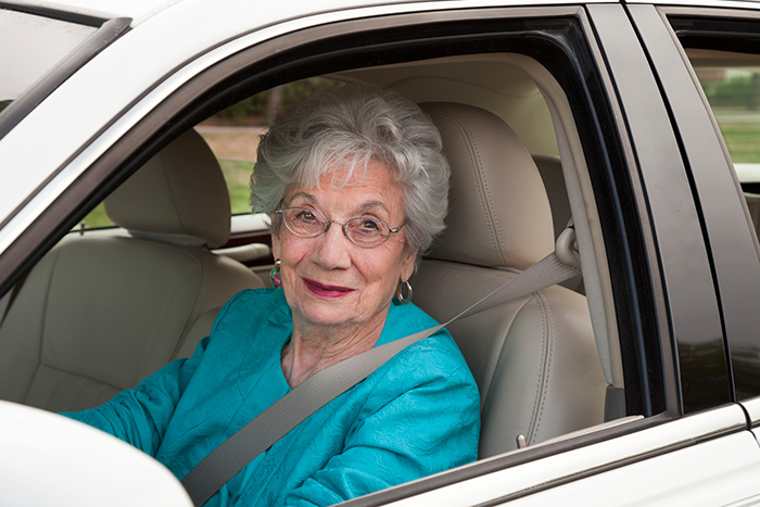 Female older driver smiling from behind the steering wheel of car