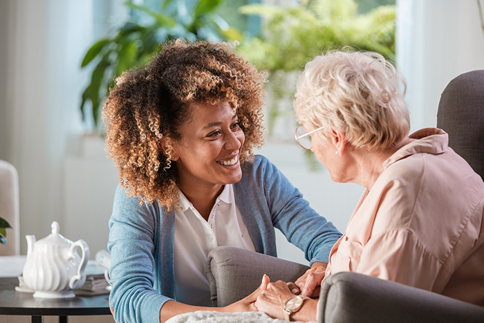 Smiling woman kneeling beside older woman sitting in arm chair