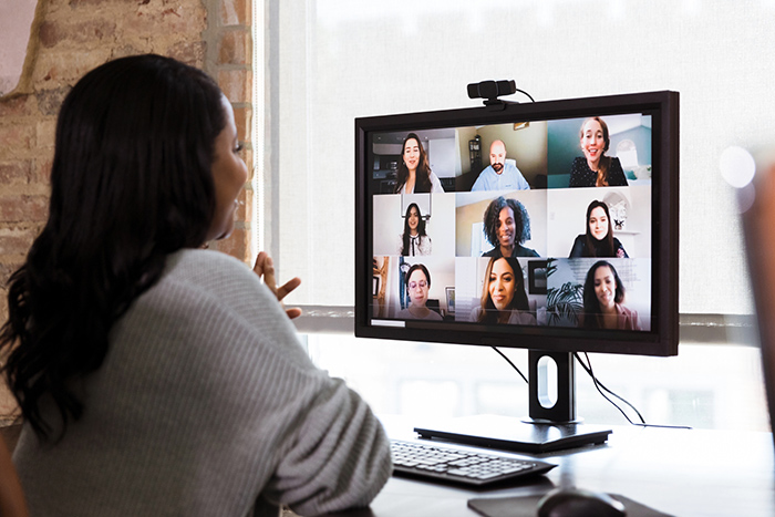 Woman sitting at desk looking at computer monitor talking to others on virtual meeting