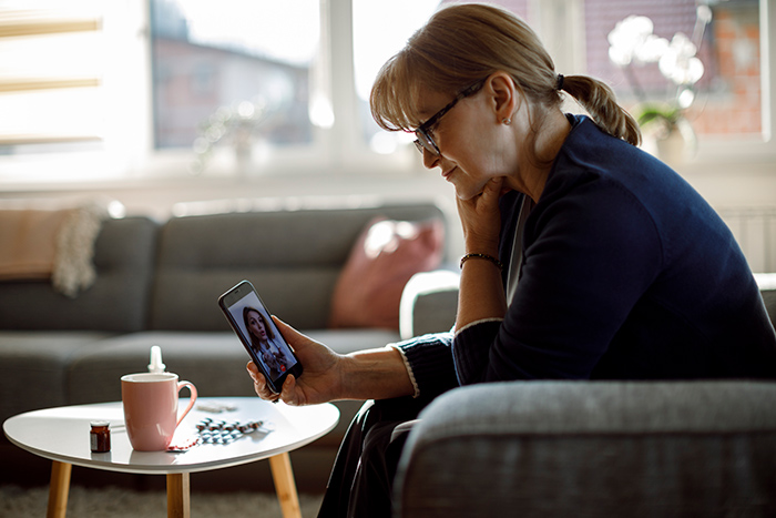 Woman sitting in chair at home looking at cell phone during telehealth conference