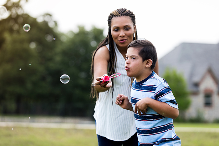 Woman outside with her young son helping him blow bubbles