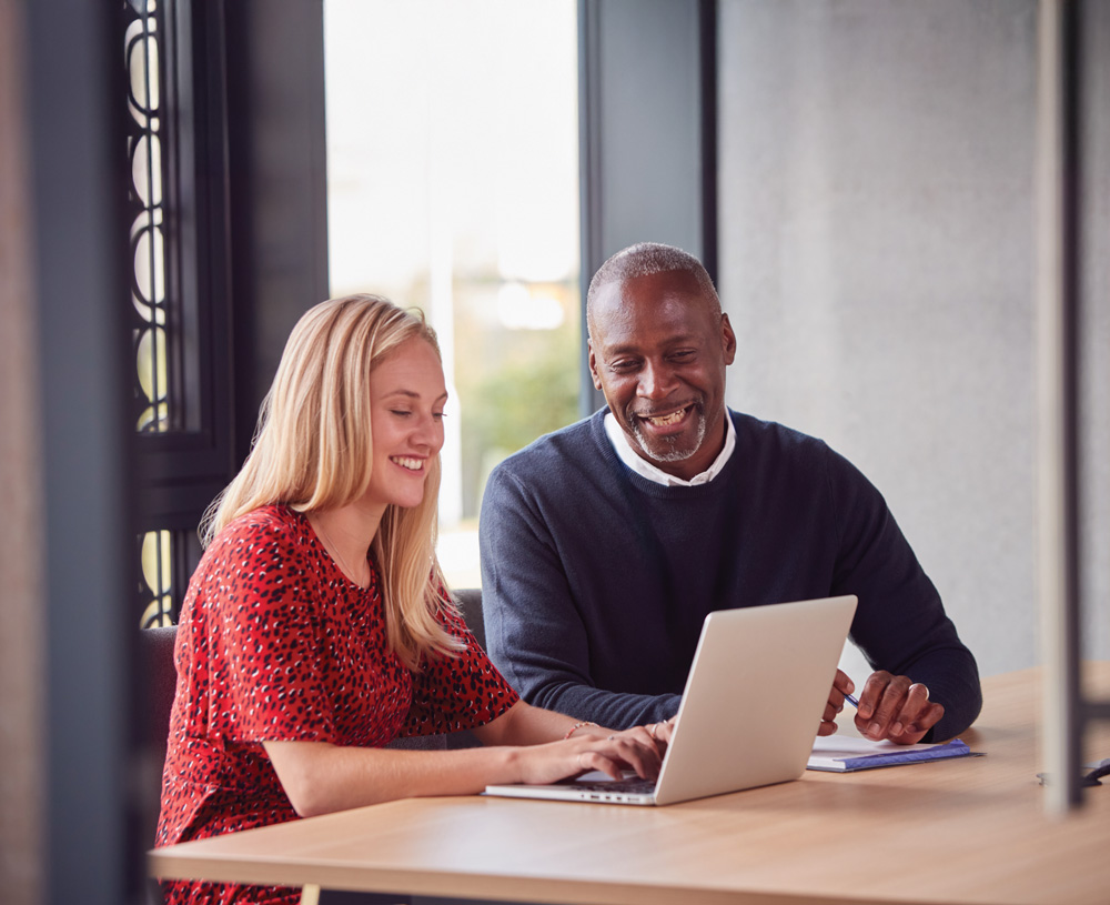 A woman and a man sitting at a table working on a laptop