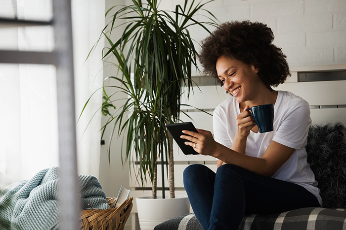 Woman sitting on couch drinking coffee and reading eReader