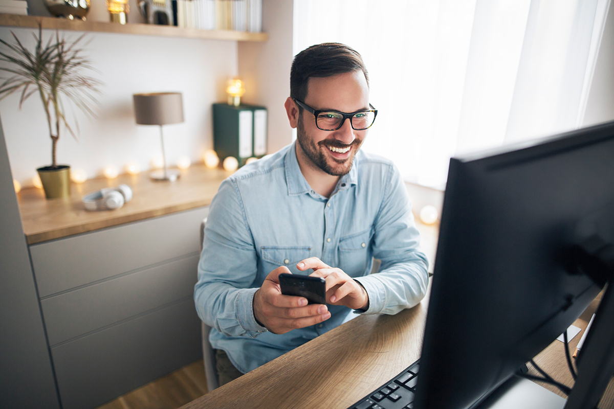 Smiling professional man looking at computer and holding mobile phone