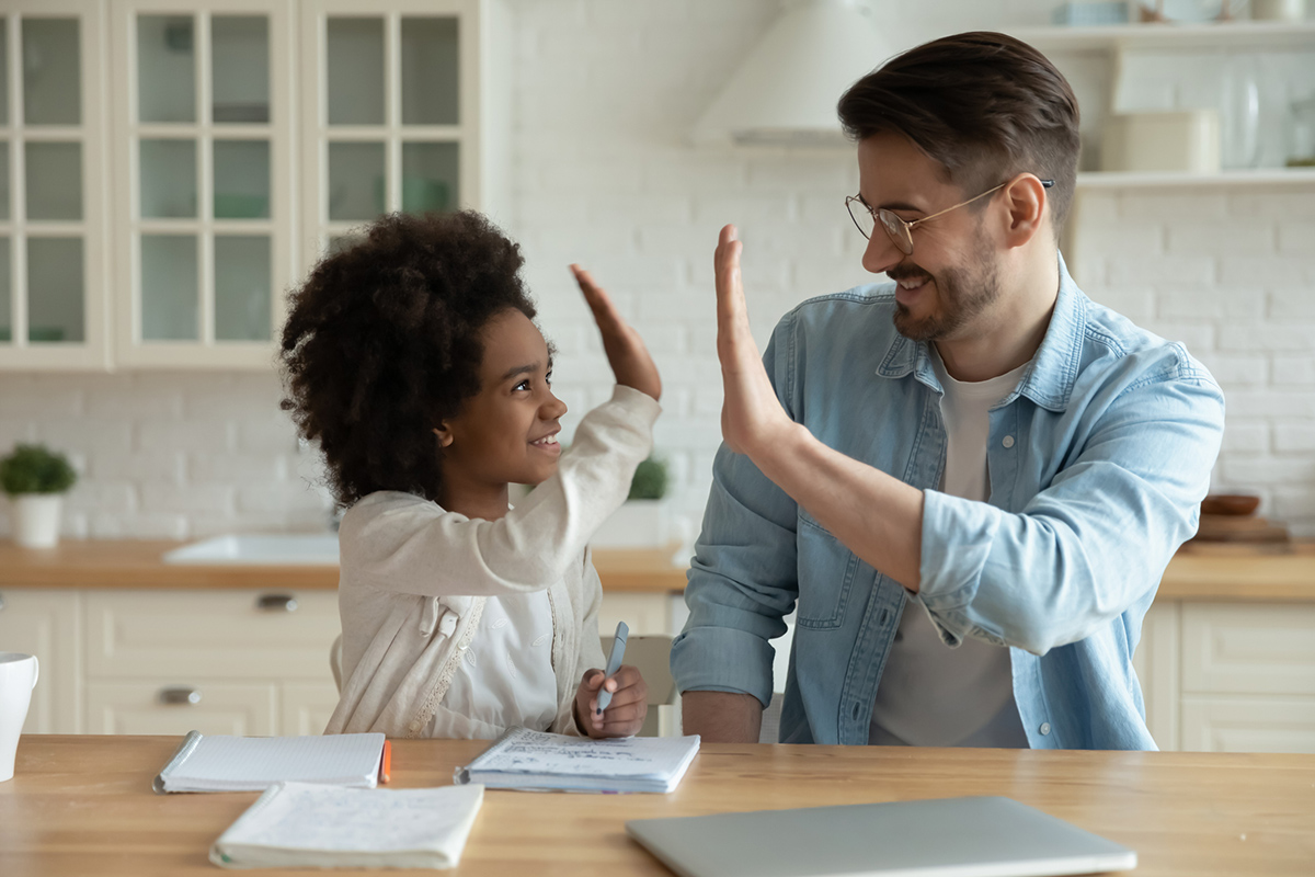 Man and young girl writing in notebook sitting at table giving a high five