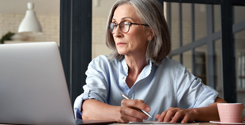 Person looking at laptop while taking notes