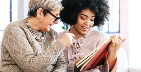 Two women sitting on a couch looking at a book.