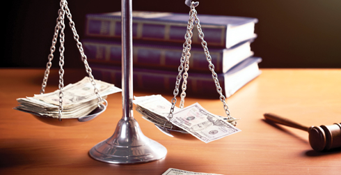 A set of metal scales with money balancing them, a gavel, and some books on a desk.
